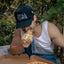 Man eating pizza outdoors wearing a 'Small Town' cap